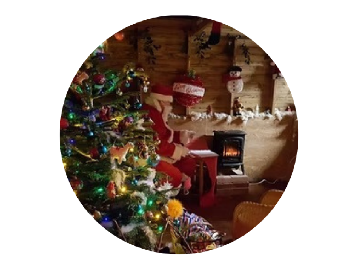 Santa sitting by a decorated Christmas tree, near a cozy stove in a festive room.