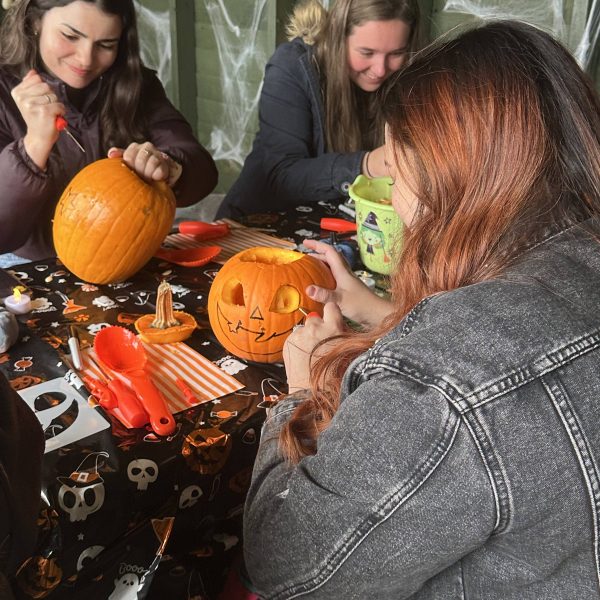 Three people carving pumpkins at a table decorated with Halloween-themed items.