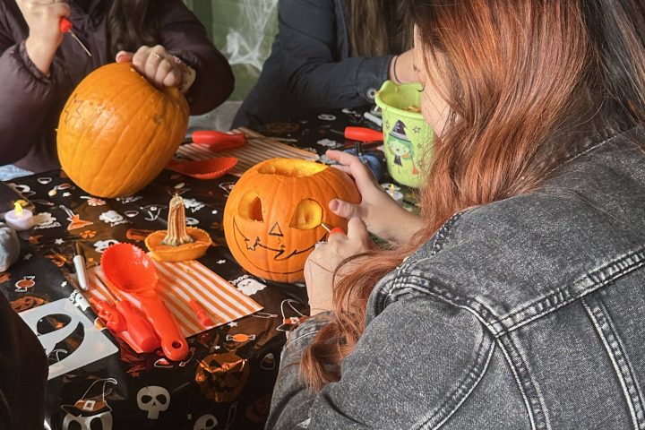 Three people carving pumpkins at a table decorated with Halloween-themed items.