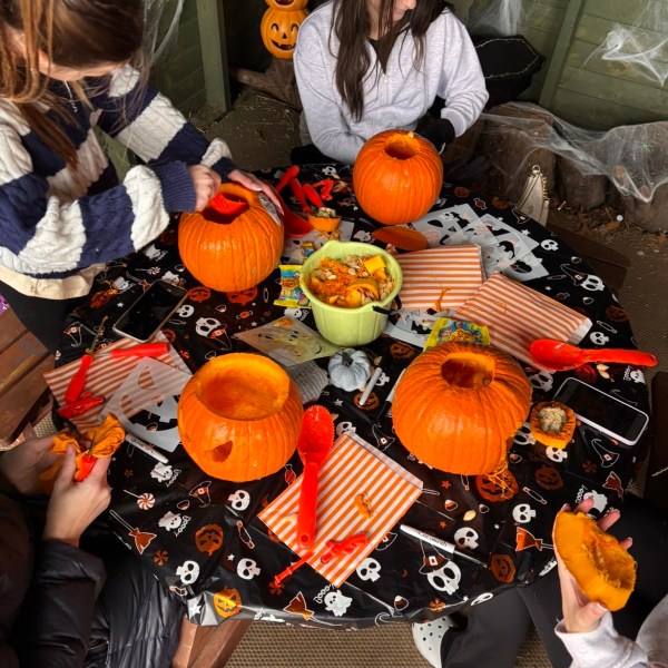 People carving pumpkins at a decorated Halloween table.