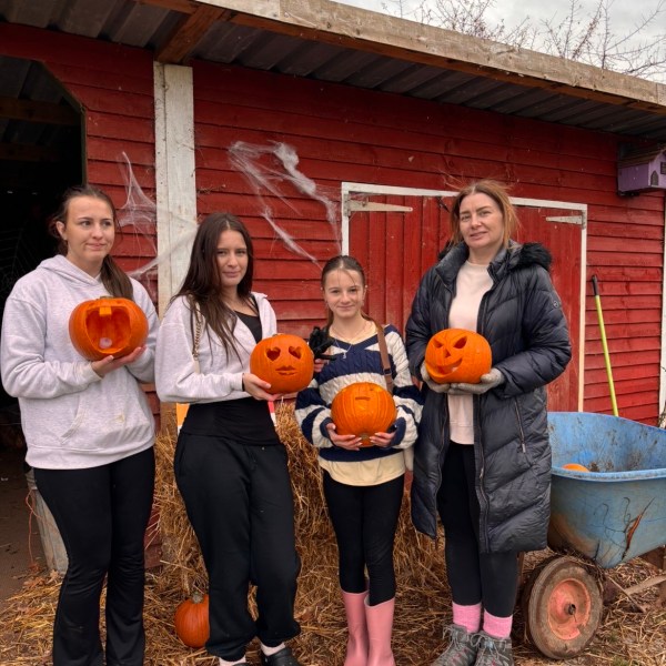 Four people holding carved pumpkins in front of a red shed on a cloudy day.