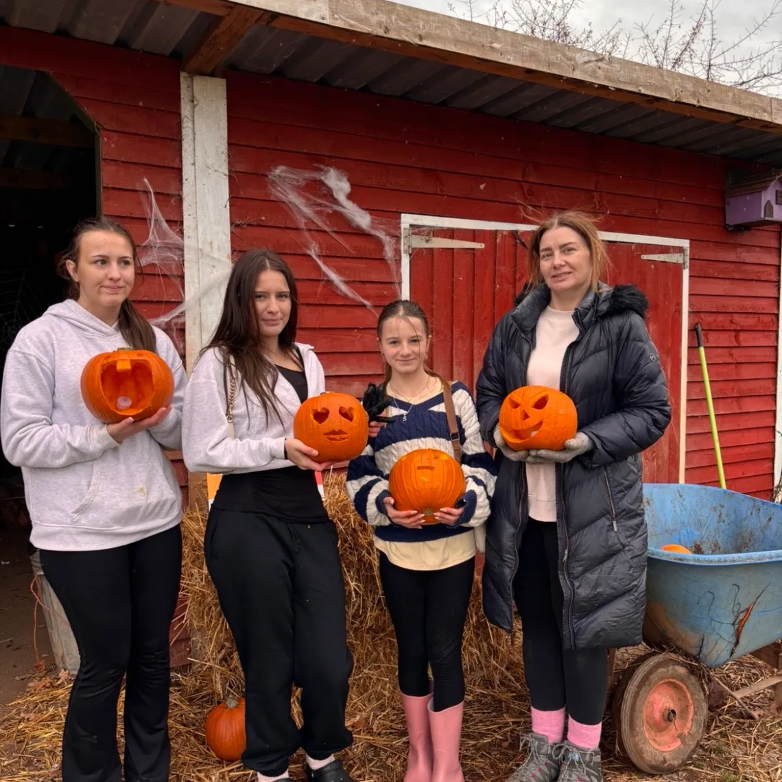 Four people holding carved pumpkins in front of a red shed on a cloudy day.