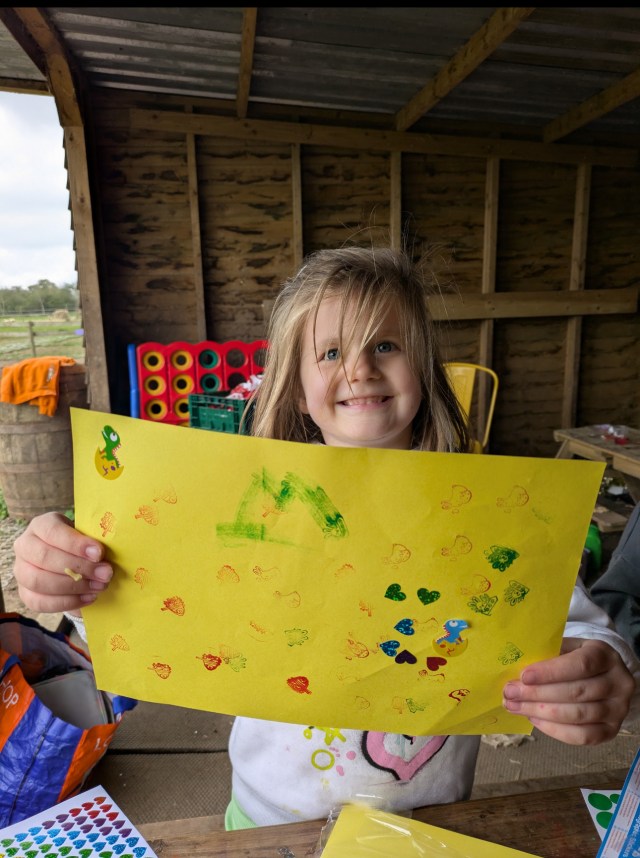 Child holding up a decorated yellow paper with stamps and stickers.