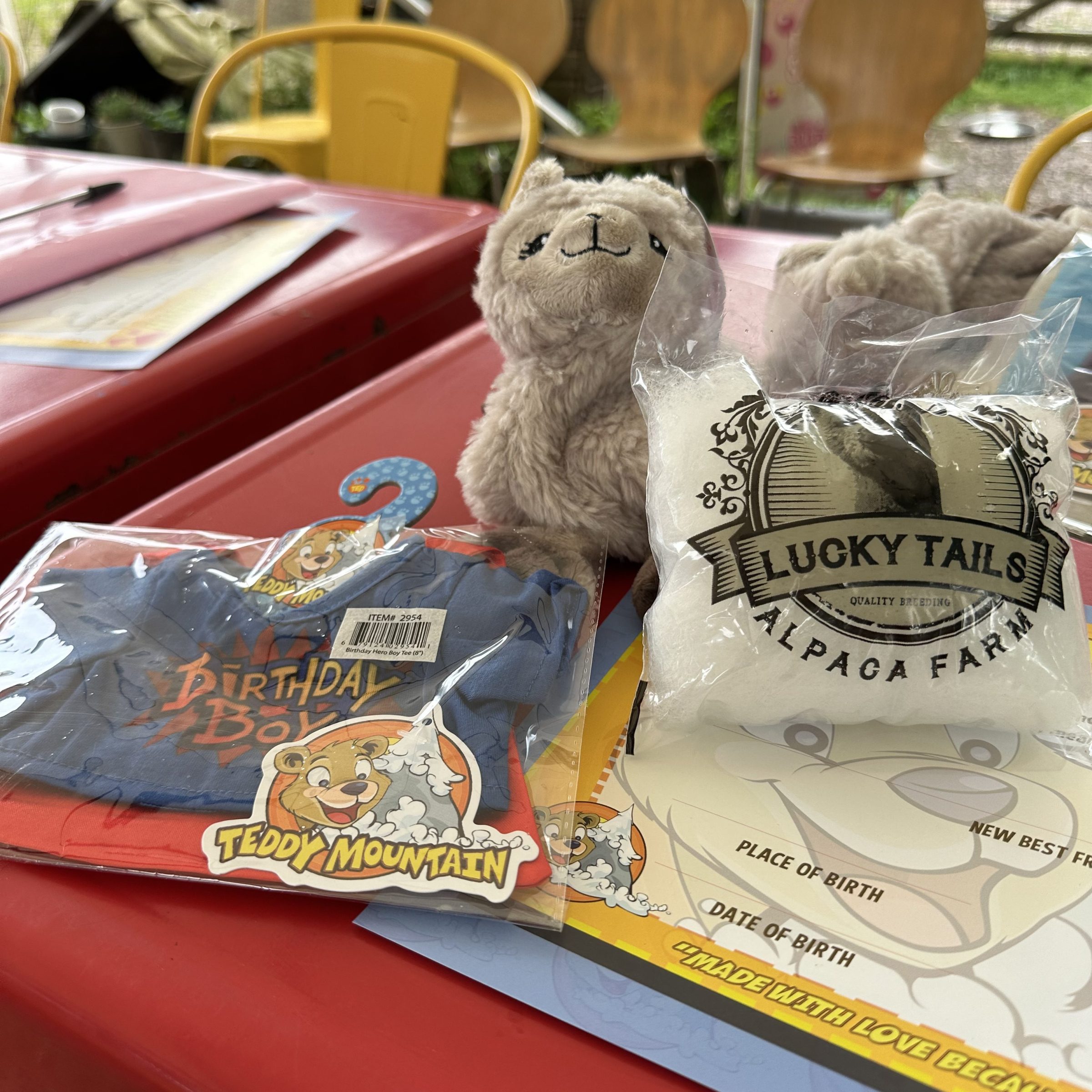 Plush alpaca toy and colorful items on a red table.